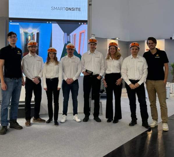 Open Experience-teamet med orangea DIGIBAU-hjälmar vid mässmontern på BAU 2025