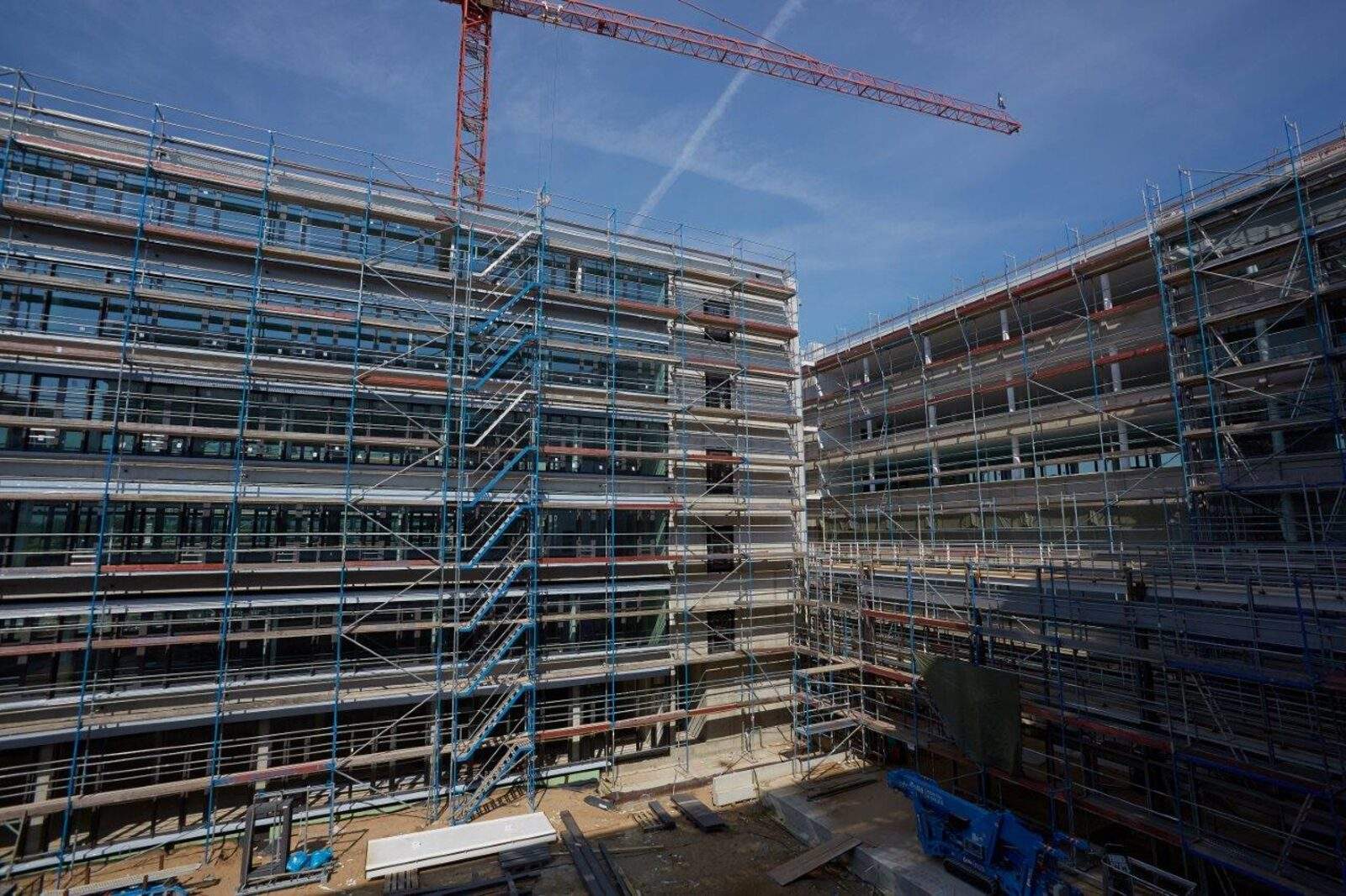 Cour intérieure d'un immeuble administratif neuf sous échafaudage, les deux ailes montrant des bandeaux d'étage régulièrement répétés, grue au-dessus du gros œuvre